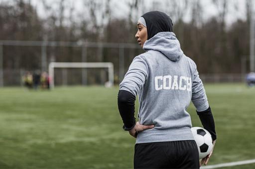 Female football coach wearing a grey hoodie that says 'Coach'