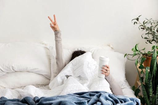 lady in bed with cover over eyes holding coffee