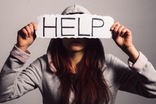 Woman holding paper sign over her face that says 'help'